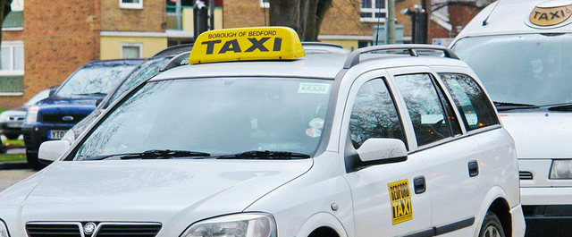 White car with a taxi sign on the top in yellow.