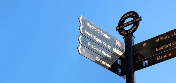 Black signpost in town showing directions to services, transport and tourist sights