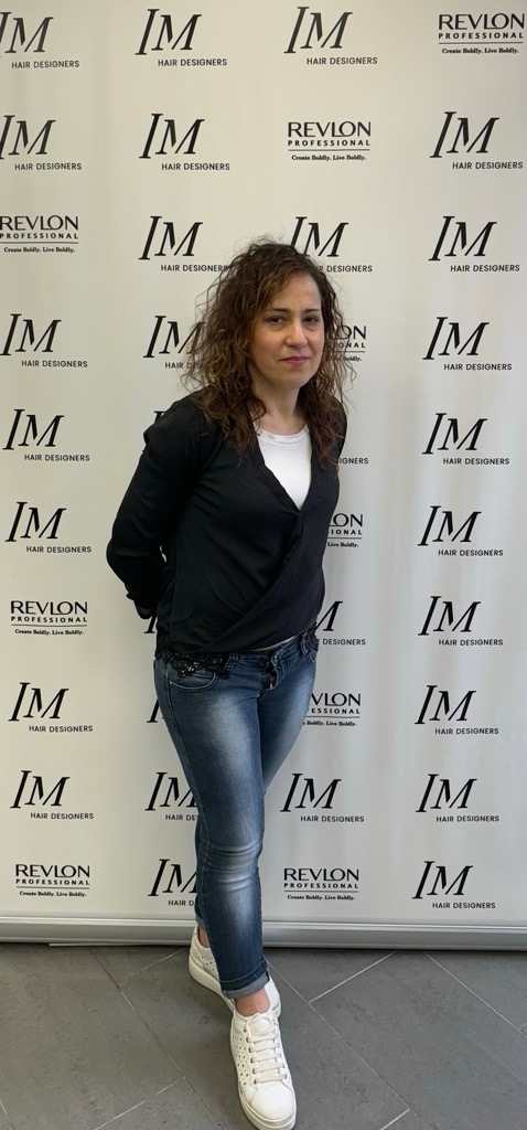 lady in a black cardiga, white t shirt and jeans stood in front of a board with logos on.