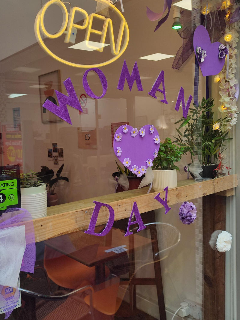 Window with the words International Women's Day in putple letters and a heart.