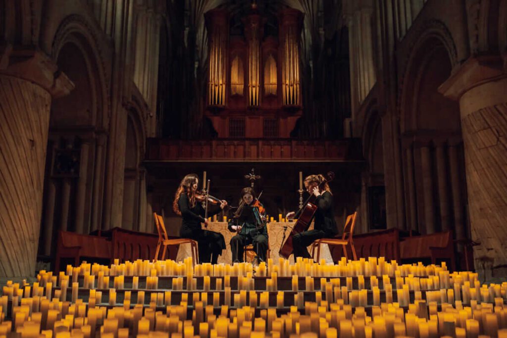 three ladies playing string instruments surrounded by hundreds of candles.