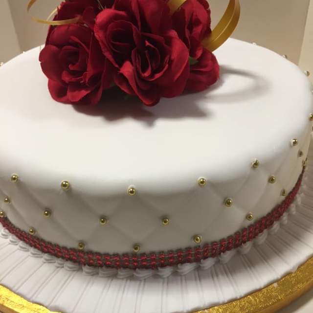 White icing covered single tier cake on a plate topped with red roses
