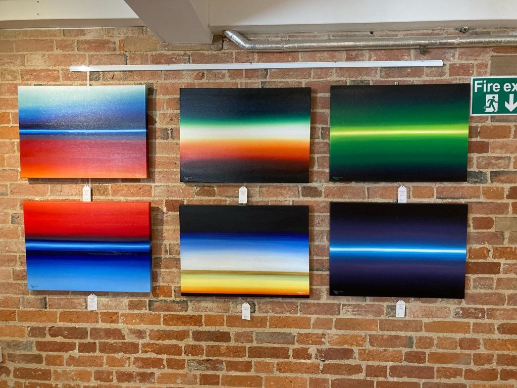 6 paintings similar images but different colours hanging on a brick wall