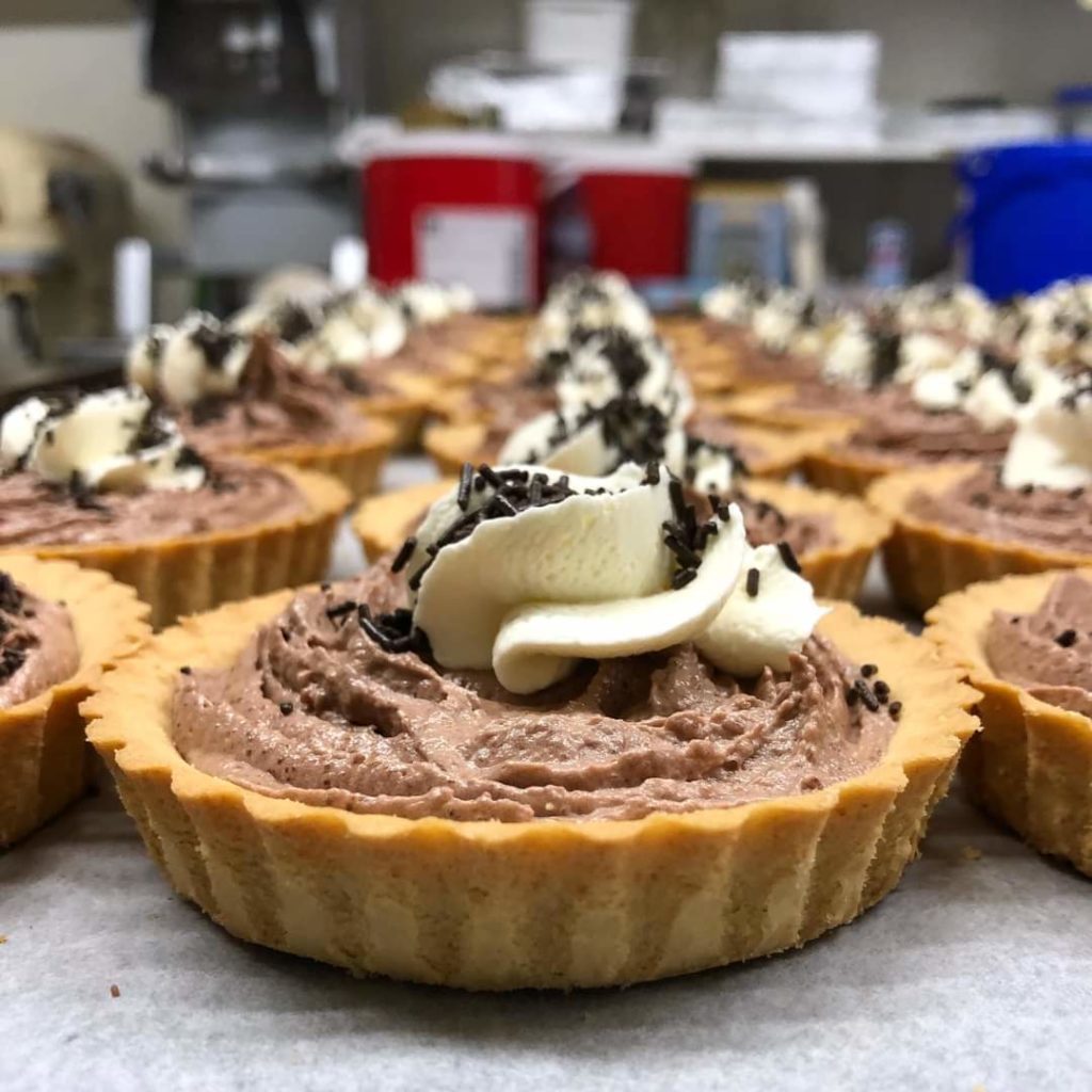 Three rows of chocolate and pastry tarts with cream swirls in the centre and chocolate sprinkles