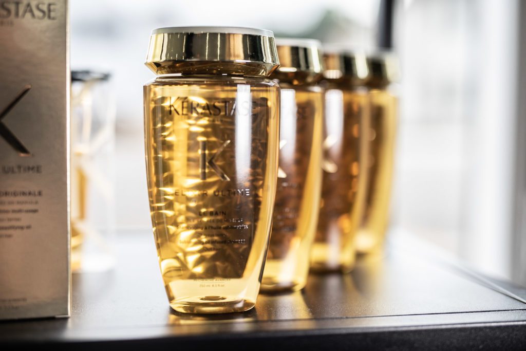 4 golden bottles of hair product in a diagonal line, with natural light reflecting off of them.