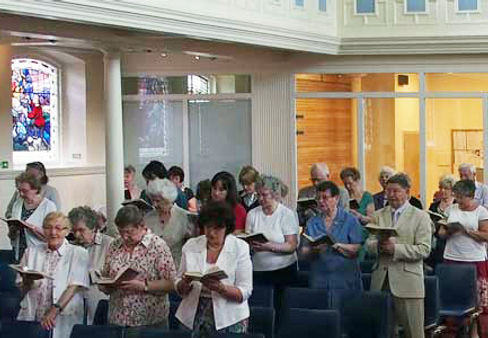 Church congregation stood in rows with hymn books singing.