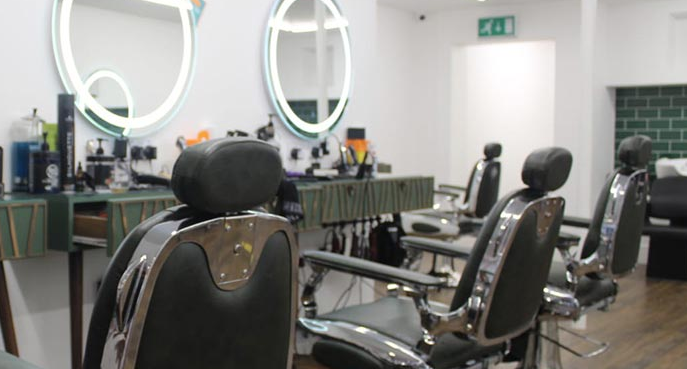 Damiano Hair salon with barber chairs. White walls with green, brick-style tiles behind wash basins