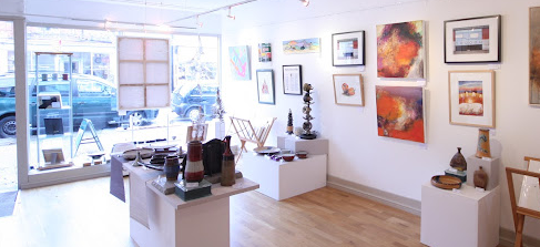 Eagle Gallery interior white with wooden floor, paintings on the wall and tables of sculptures