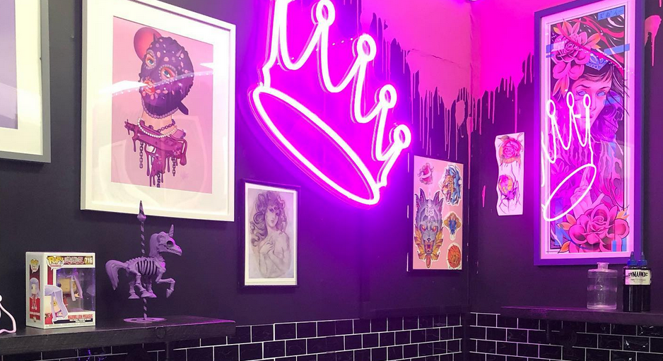 Four Kings studio with black painted walls and black brick-shaped tiles with fluorescent pink word lights and brightly colour tattoo images