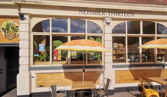 Green Earth Cafe shopfront with green and gold branding and orange segment printed umbrellas