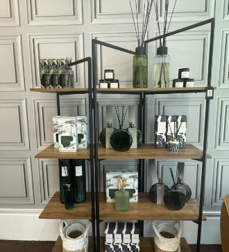 Diffusers and candles on wooden shelves with a black frame.