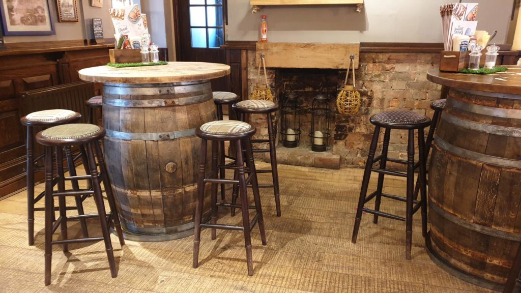 Two large barrels converted into tables, next to a fireplace. bar stools surround the tables.