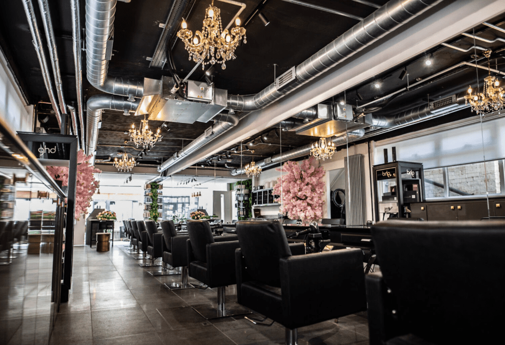 Interior picture showing a row of leather chairs in front of mirrors, golden chandeliers hanging from the ceiling and 2 pink blossomed trees