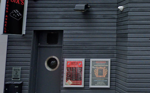 Six's external shot with grey timber panelling, round window in door and posters showing what's on