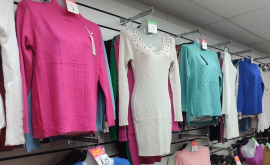 a pink jumper, a white dress, a turqoise jumper and a blue jumper hanging up on a wall.