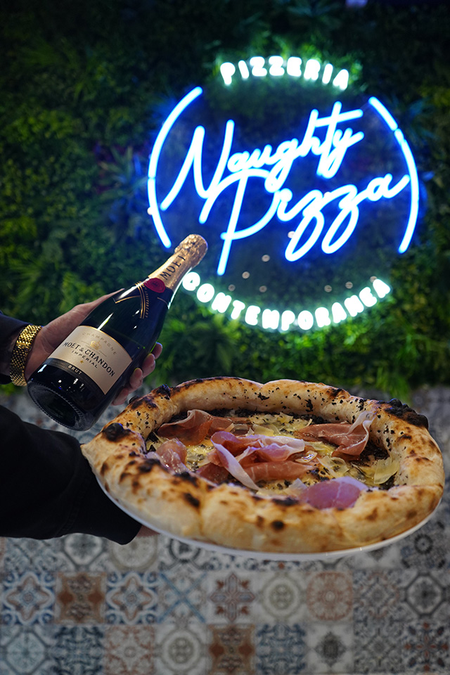 Naughty Pizza blue neon sign on living wall with champagne and fresh pizza