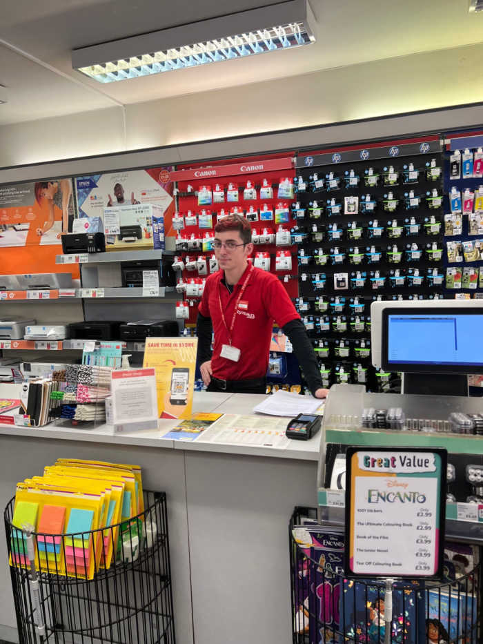 Main service counter, employee stood at checkout, products lining the wall behind him.