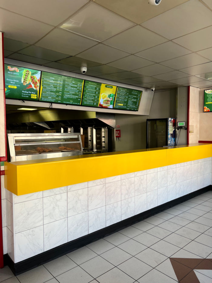 Main service area. White tiles and yellow counter top. Green menu display boards above.