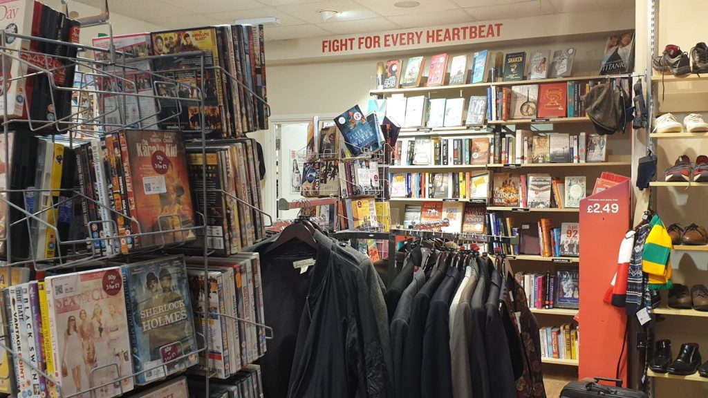 DVD circular rotating rack in foreground, a circular clothes rack with mens jackets and bookshelves at the rear