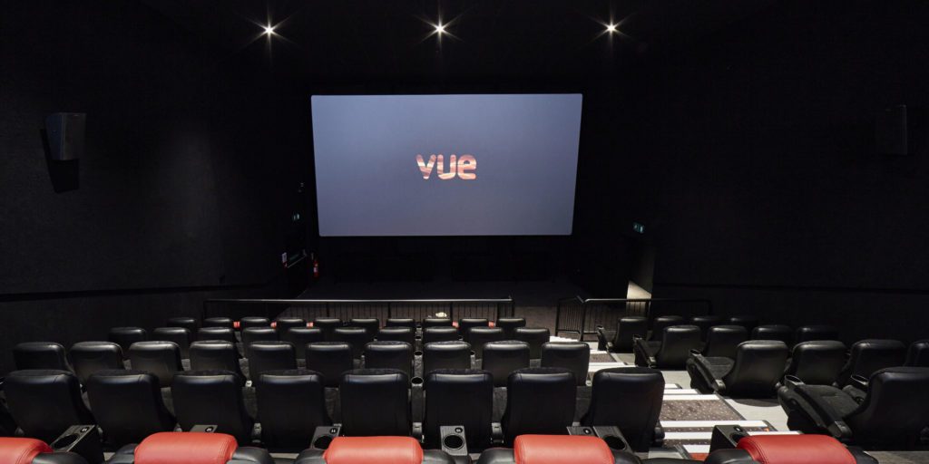 A dark room with red and black chairs facing a screen with the 'Vue' logo on it.