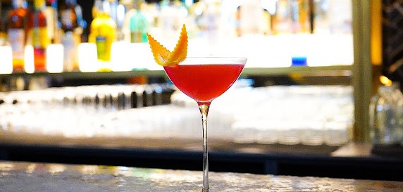 Cocos bar with elegant glass with pink cocktail and orange peel garnish