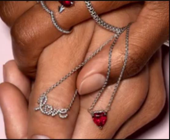 Hands holding silver necklaces with the word love as a pendant in diamonds