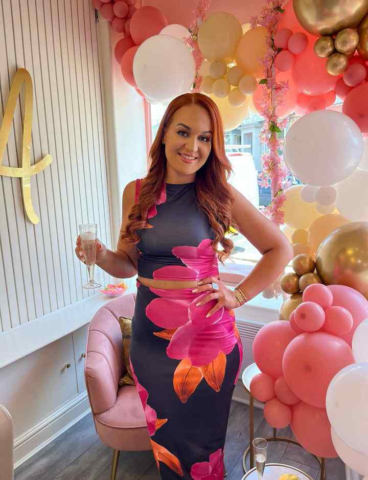 Lady wearing a pretty flowery dress. With long auburn hair. Surrounded by pretty balloons.