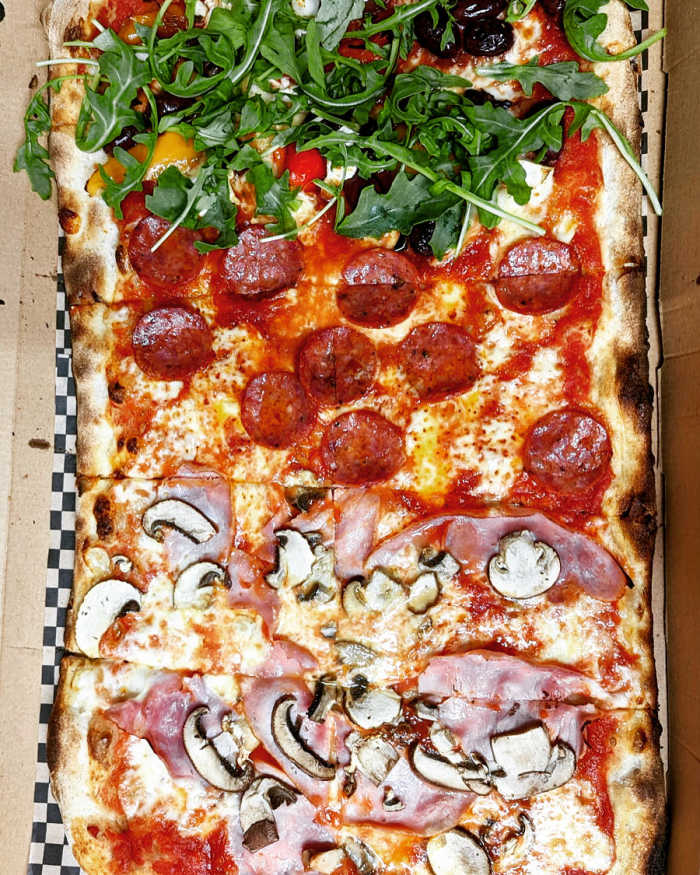 Rectangular pizza with ham, mushroom, pepperoni and rocket toppings.