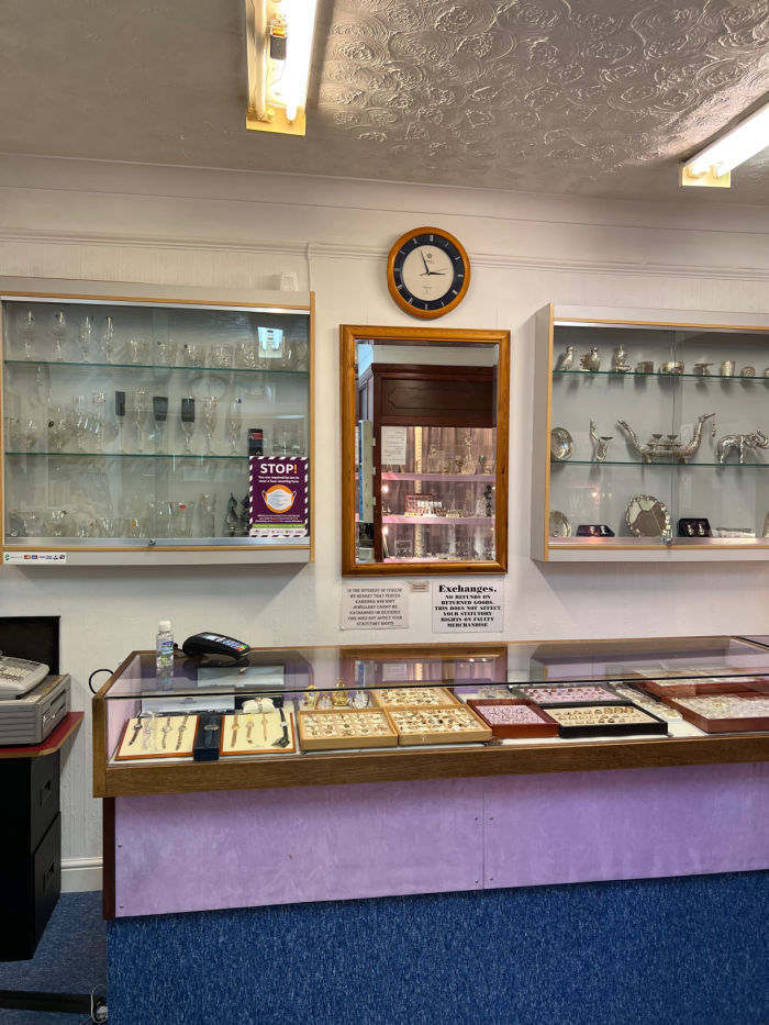 Service counter, glass case top with Jewelry on display. Mounter wall cabinets behind displaying more items.