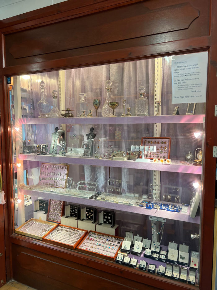 Large wood and glass display case with side lighting displaying jewelry.