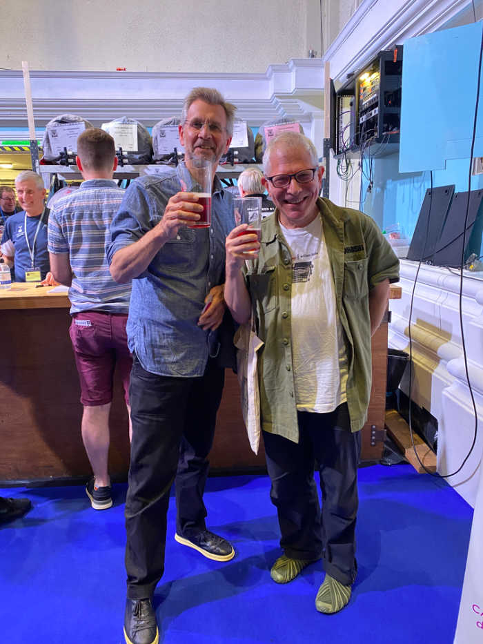 Two gentlemen standing in front of a bar holding beers at the Beer & Cider Festival