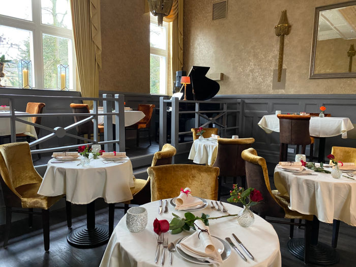 A posh dining room with tables with white cotton tablecloths and a red rose on each table.