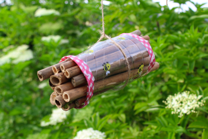 A home made bee house handing against a background of grass and white flowers