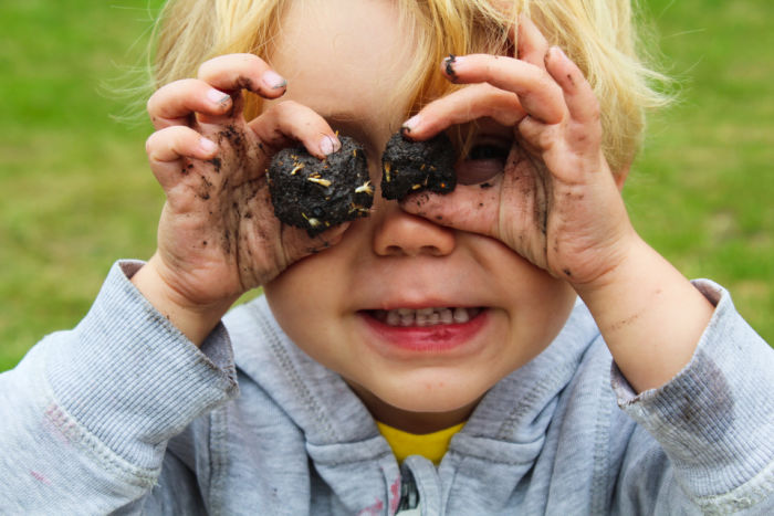 Small child holding two balls of dirt like binoculars