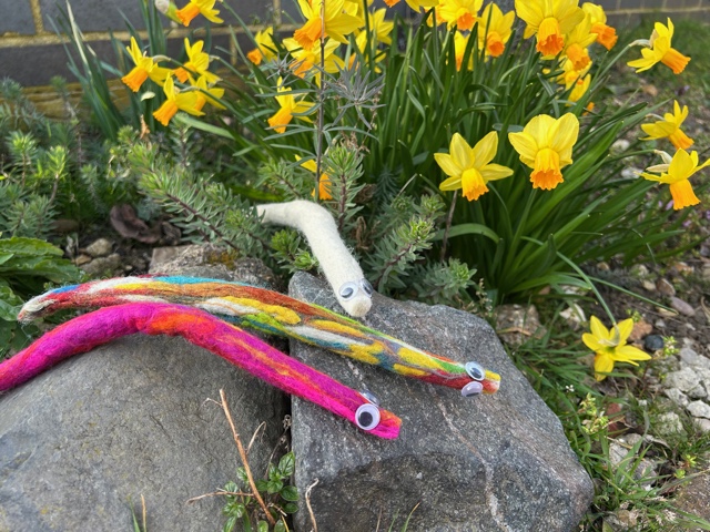 hand made craft worms on a stone surrounded by daffodils.